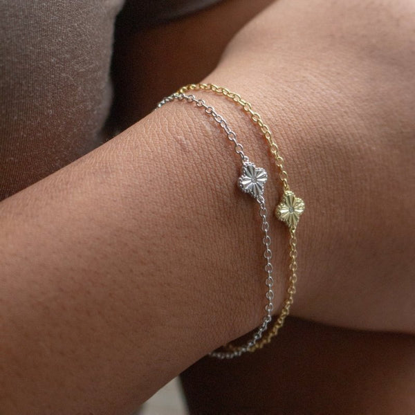 Close-up of a wrist wearing two bracelets with clover designs.