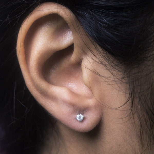 Close-up of an ear wearing a diamond stud earring against a dark background