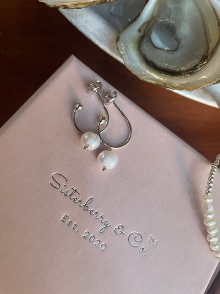 Silver hoop earrings with white pearl drops, displayed on a pink branded jewelry box with 'Sutterberry & Co. Est. with oysters in the background