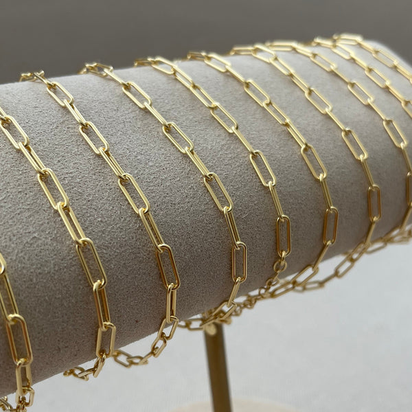 Gold chain bracelet on a gray cylindrical stand with a white background