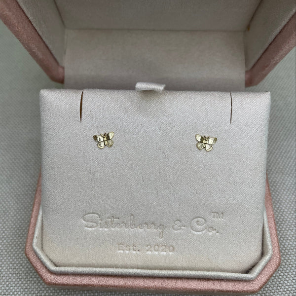 Gold earrings in a pink jewelry box on a gray surface