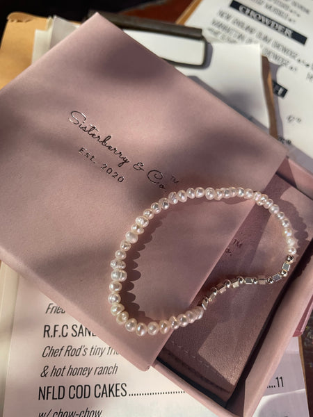 A pearl beaded bracelet with silver-toned metal links and a clasp, displayed inside a pink presentation box with a branded paper insert. The visible brand on the insert reads Sisterberry & Co.