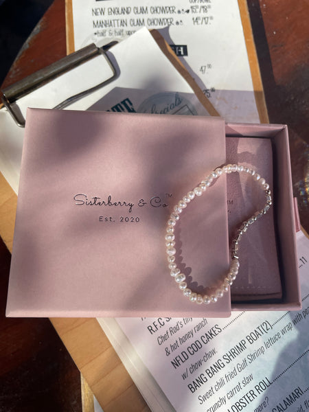 A pearl beaded bracelet by Siantanberry & Co. resting on its dusty pink presentation box, which is placed on top of receipts on a wooden table.