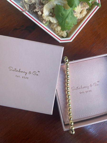 Blush pink Sisterberry & Co box with 6mm round ball beaded bracelet with fried calamari and cilantro in the background. 