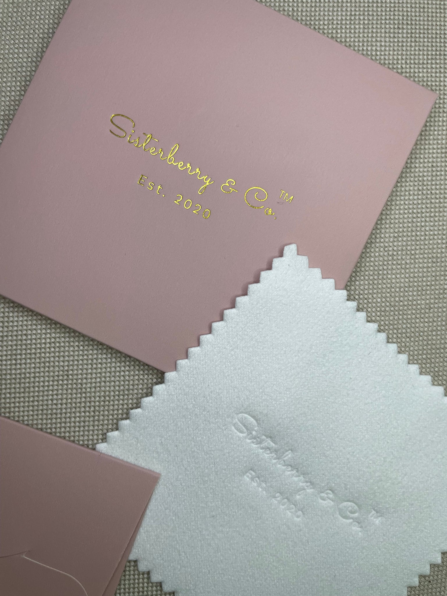Pink card with gold text and white swatch on a textured surface