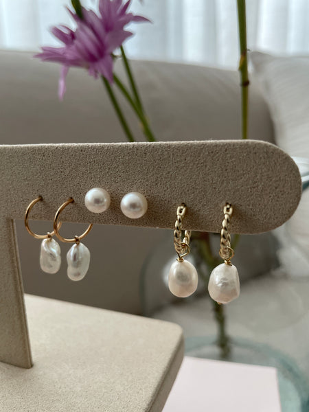 Gold and pearl earrings on a display stand with a blurred background