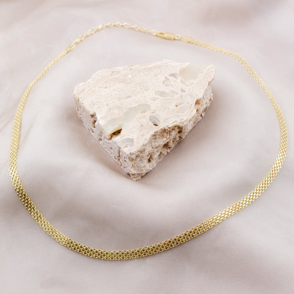 Gold chain necklace draped over a piece of white fabric on a light background