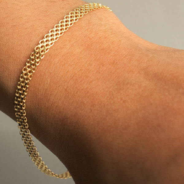 Gold chain bracelet on a wrist with a neutral background