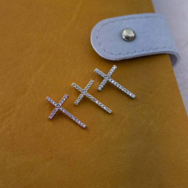 Silver cross-shaped earrings on a yellow surface with a light blue strap in the background.