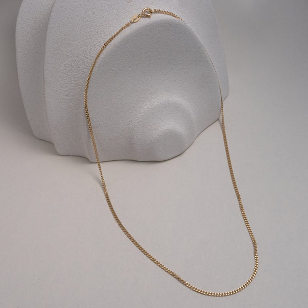 Gold chain necklace on a gray stand with a plain background