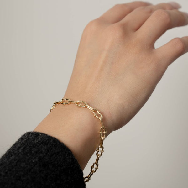 Gold chain bracelet on a wrist against a neutral background