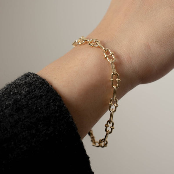Gold chain bracelet on a wrist against a neutral background