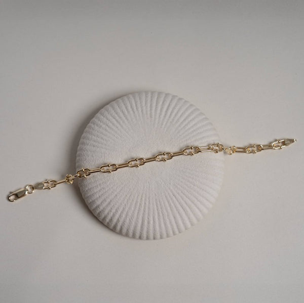 Gold bracelet on a white shell against a light gray background