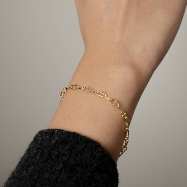 Gold chain bracelet on a wrist with a neutral background