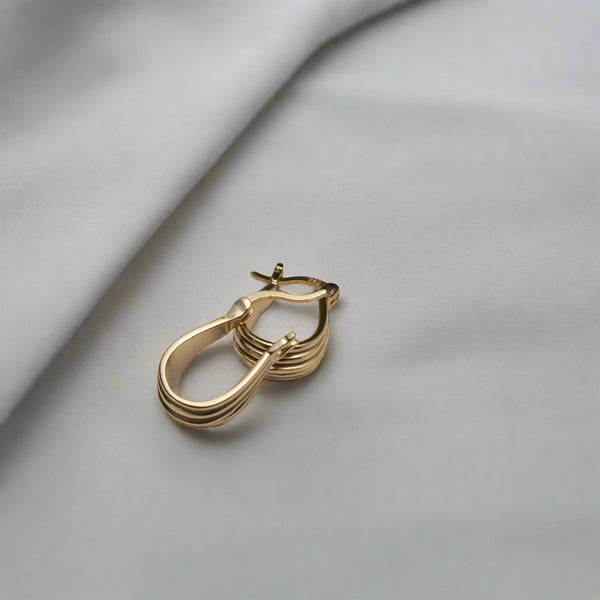 Gold hoop earrings on a light gray surface with a eucalyptus leaf.