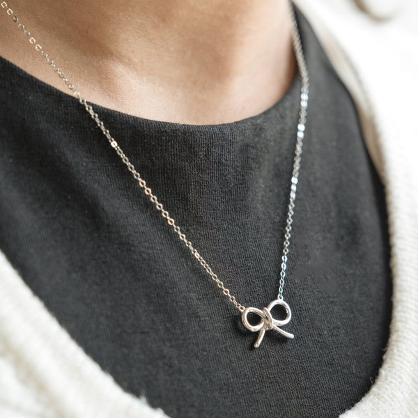 Necklace with a bow pendant worn by a person on a dark background