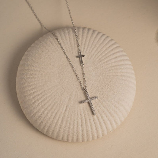 Silver cross necklace on a shell with a beige background