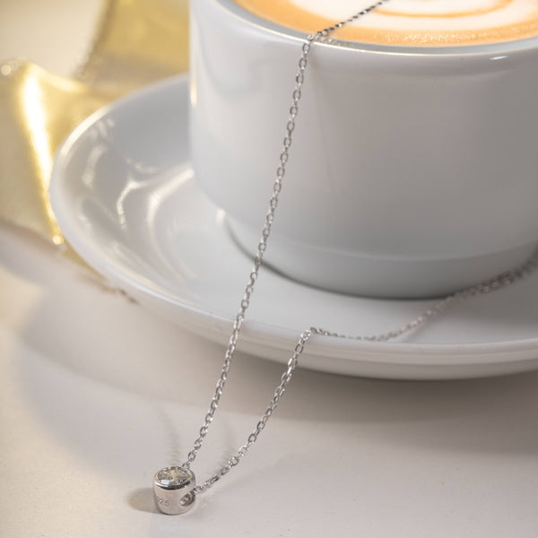 Silver necklace with a small round diamond bezel pendant on a coffee mug