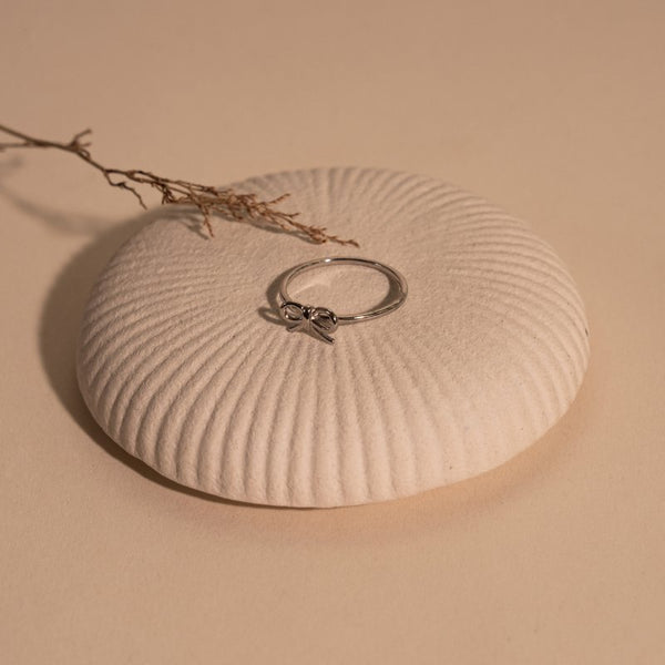 Silver ring on a textured beige surface with a branch