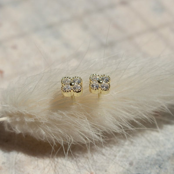 Gold square stud earrings with clear gemstones on a soft white fur background