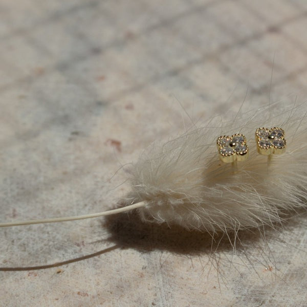 Gold earrings with gemstones on a fluffy white plant stem against a neutral background