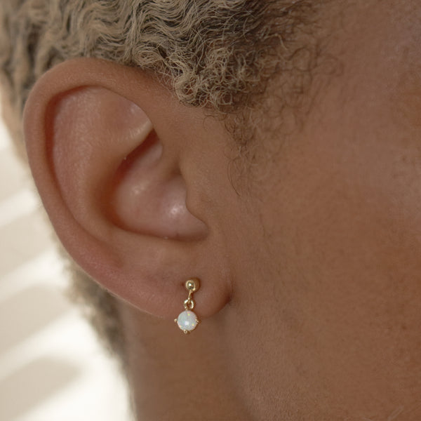 Close-up of an ear wearing a gold earring with a small pearl.